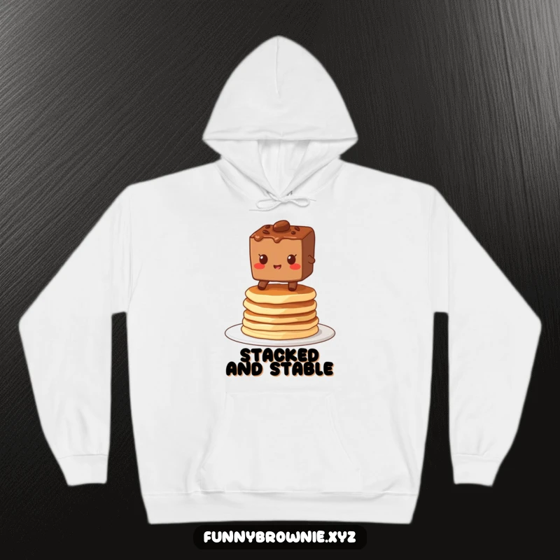 Funny hoodie depicting a brownie character grinning while balancing on a wobbly stack of pancakes, perfect for cozying up.